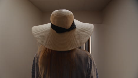 a woman in a sun hat walks down a hotel hallway