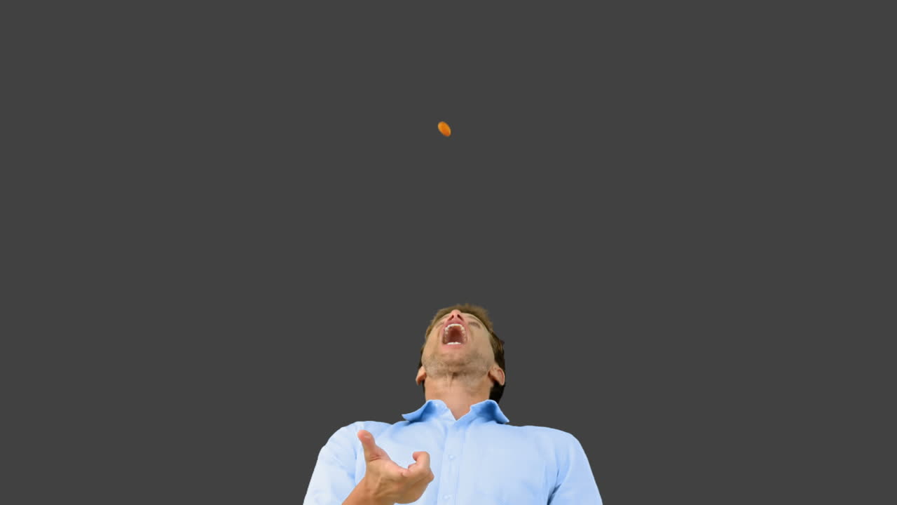 Man catching an orange segment with his mouth on grey screen