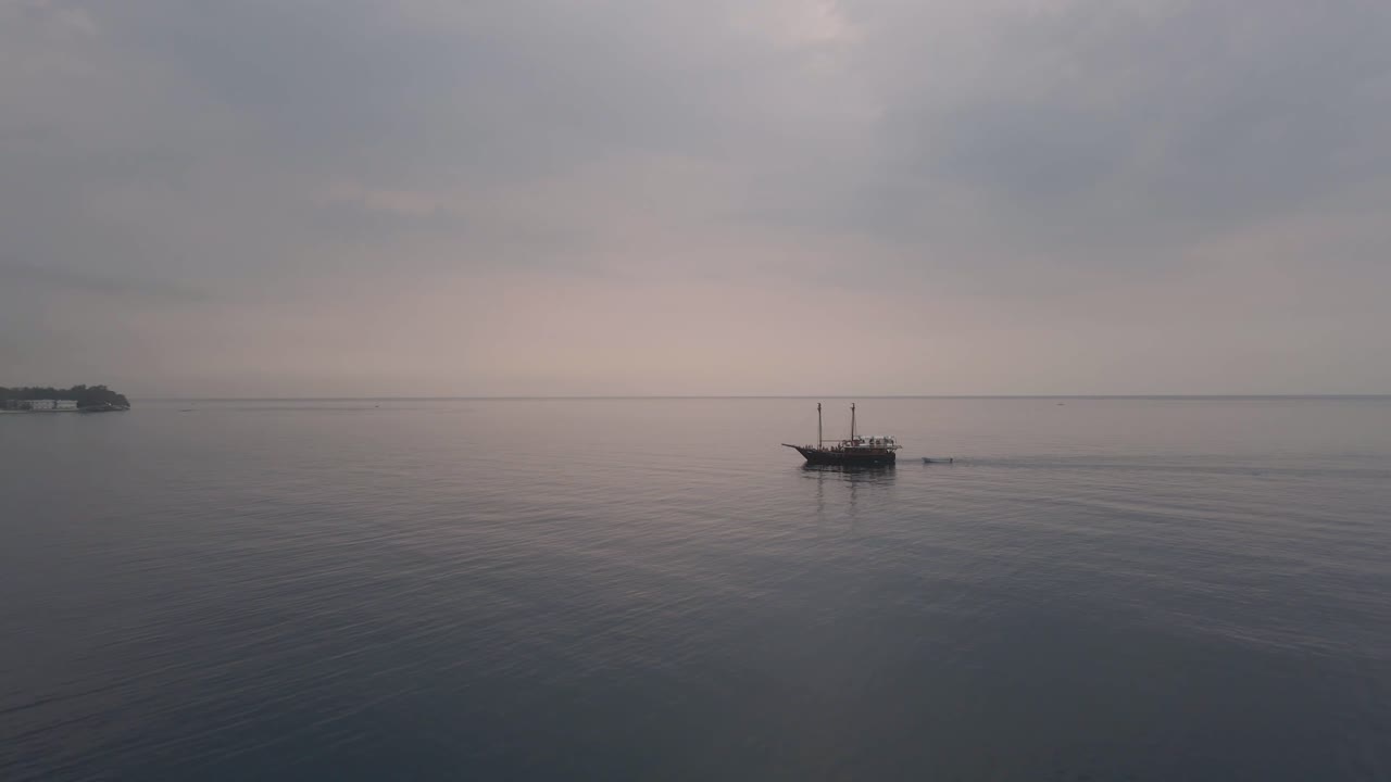 Drone video showing solitary sailboat floating on calm water under soft overcast sky near Amed Coast, capturing peaceful seascape, gentle movement, and quiet coastal atmosphere in Bali Indonesia
