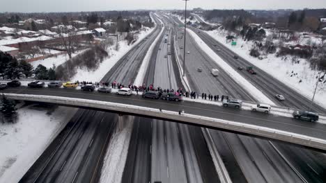 los manifestantes canadienses ondean banderas en un día ventoso, de pie al borde del paso elevado de la autopista concurrida
