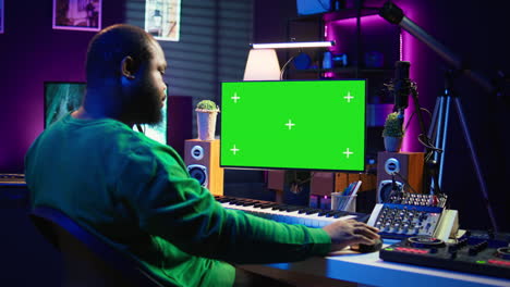 Producer-composing-music-with-electronic-keyboard-notes-and-green-screen-display