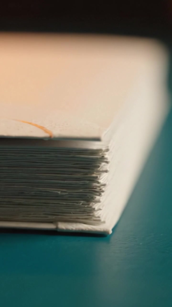 Close-Up Perspective of a Book's Edge and Binding, Focusing on Textured Cover and Pages Set Against a Blue Surface with Warm Ambient Lighting