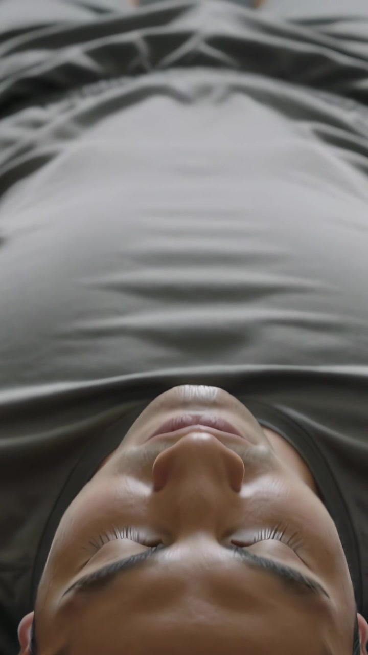 Lodret video: Kamera trækker sig tilbage, voksen mand ligger stille hjemme på sengen, viser grå T-shirt og shorts