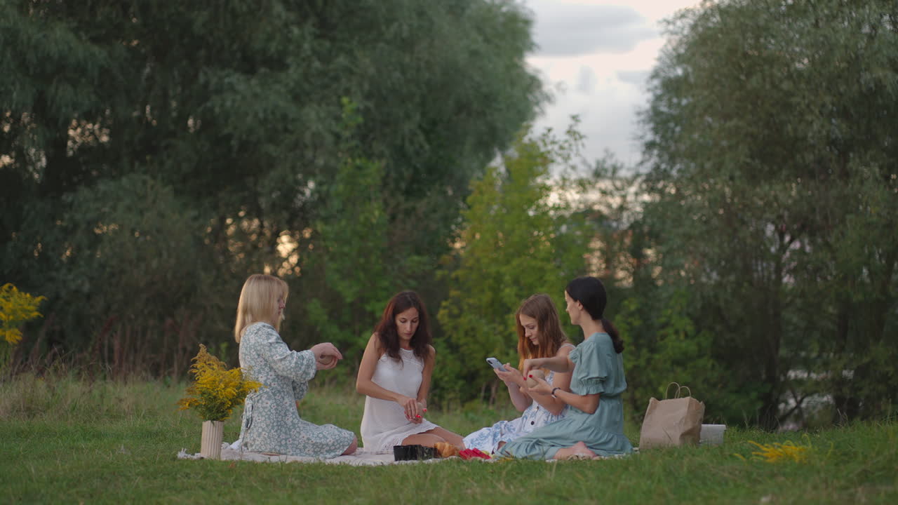 Young women conduct clay modeling classes in the open air. One girl takes notes on her smartphone conducts correspondence online. Communication hobbies women's circle creative activity.