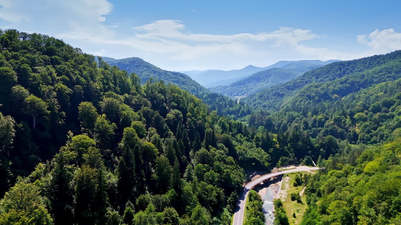 Scenic view of a lush valley with winding road. A stunning aerial view captures a vibrant valley surrounded by mountains and greenery under a clear blue sky