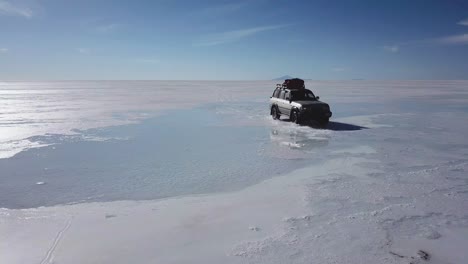 Drone-following-a-car-driving-on-Uyuni-Salt-Flat,-Salar,-Bolivia