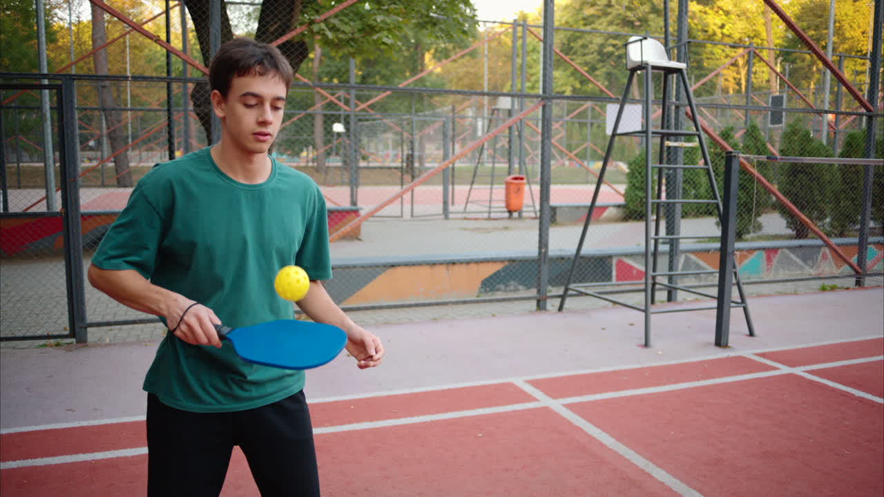 Boys playing pickleball with yellow ball and blue paddle at a court