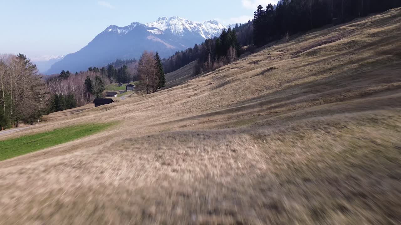 drones vuelan a lo largo de un campo con pequeñas chozas con pintorescas montañas cubiertas de nieve en el fondo en austria