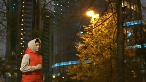 la cámara se enfoca en una mujer con ropa deportiva y capucha corriendo en la ciudad por la noche en invierno