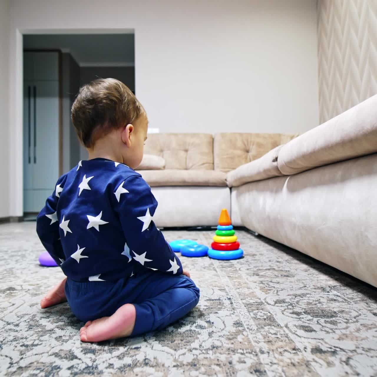 Lovely child lies on the floor looking under the sofa. Kid rises and sits on his knees. Black cat sitting behind watching a baby