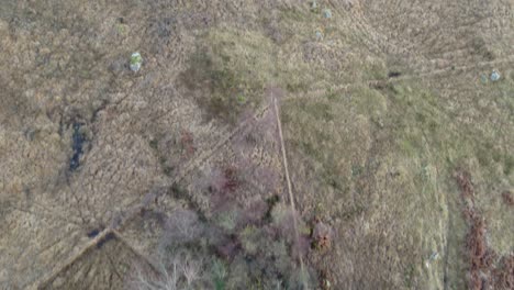 Aerial-drone-footage-flying-forward-over-fields-and-a-remote-single-track-road,-slowly-tilting-to-reveal-Glen-Etive-and-Loch-Etive-in-the-Highlands-of-Scotland-with-snow-capped-mountains-and-a-forest