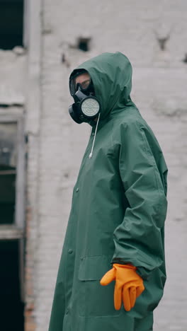 perplexed survivor in abandoned place. human in safety uniform and gas mask standing alone and looking to the sides on the background of destroyed buildings. vertical video