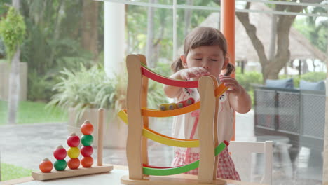 cute multiethnic preschool kid girl playing pushing cars on racing ramp to follow course of tracks in slow motion