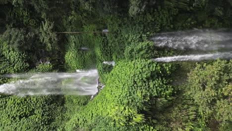 Vertical-format-aerial-ascent-up-lush-jungle-waterfall-foliage,-Lombok