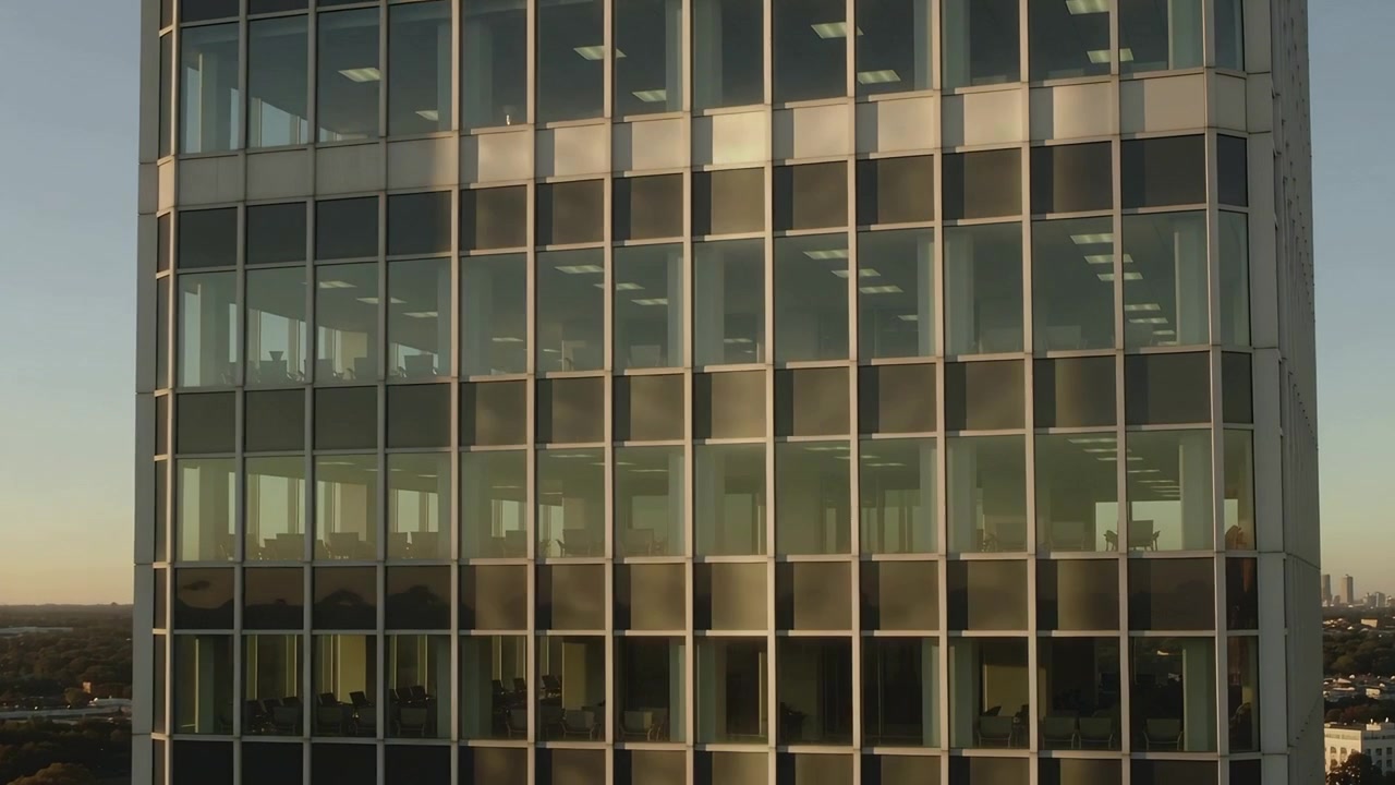 Fachada de cristal de oficina reflejando el resplandor cambiante y mostrando escritorios, luces durante la hora dorada mientras el sol se mueve