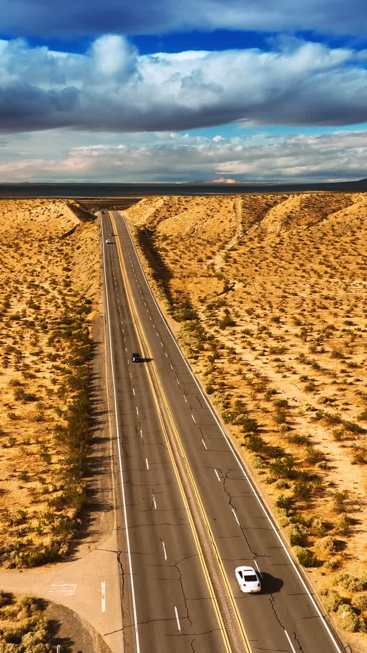 Drone moving above the four-lane highway in the dry desert. Arid landscape in California. Dramatic cloudscape in the sky at backdrop. Top view. Vertical video