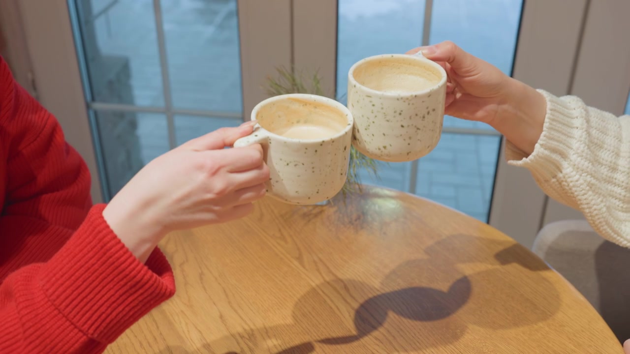 Young Woman Sips Coffee After Clinking Mugs with Friend