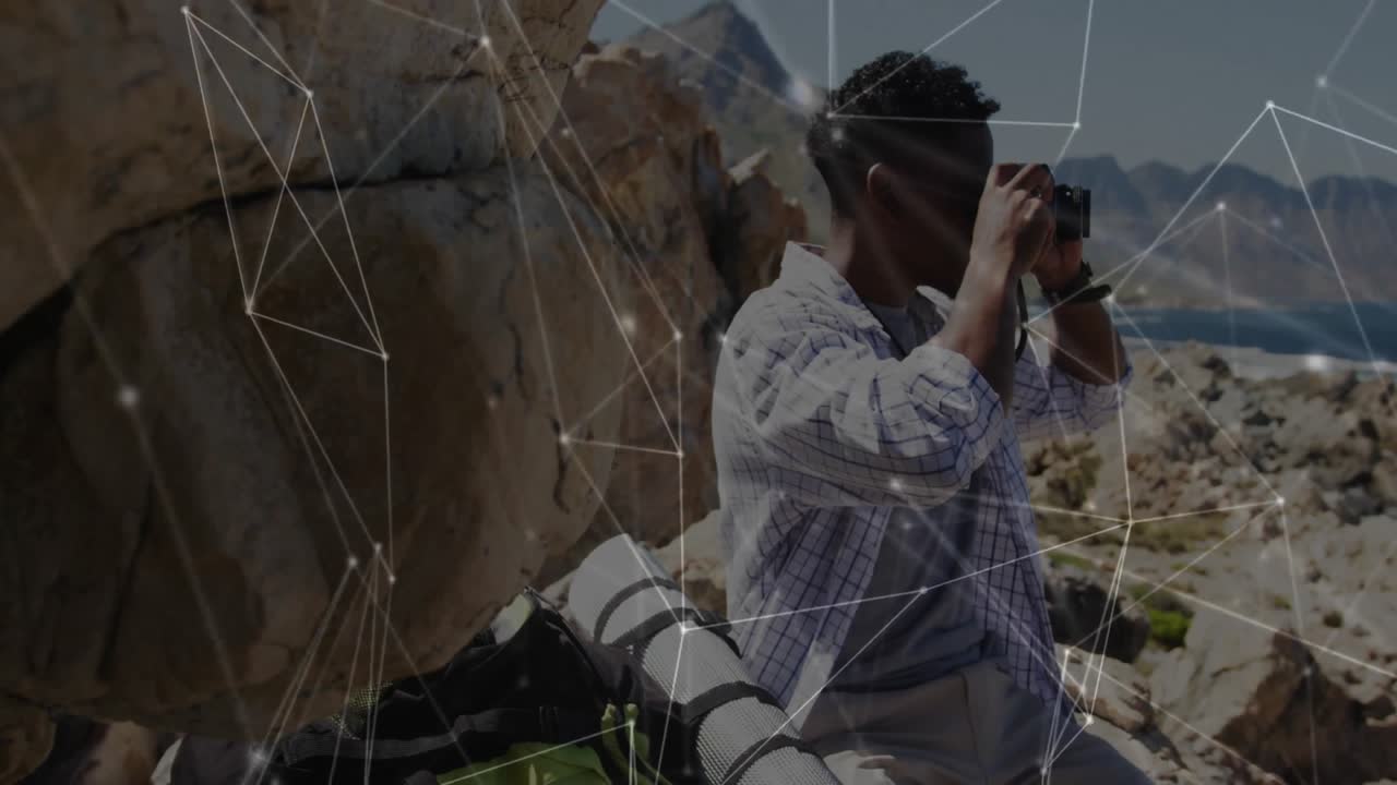 Man grabbing camera on canyon ledge and capturing lake view while tech graphics floating