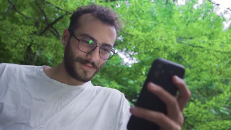 Young-man-looking-at-phone-under-trees.