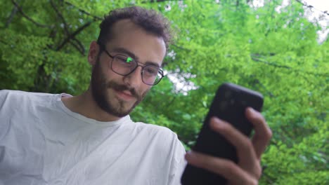 joven mirando el teléfono debajo de los árboles.