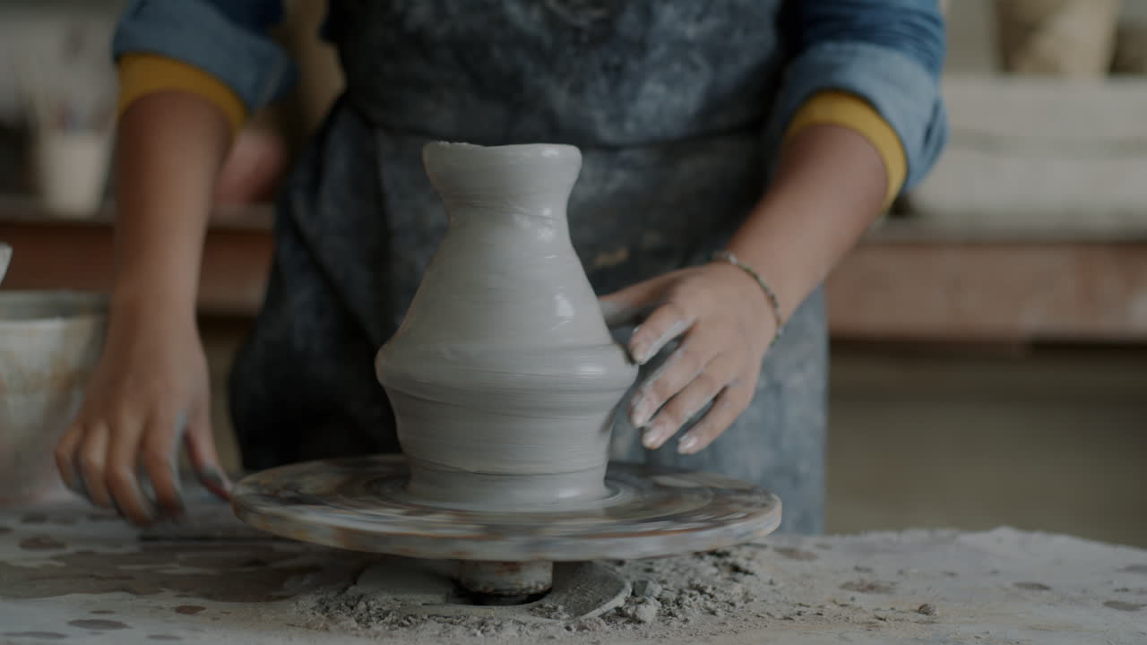 Woman shaping a clay pot on a pottery wheel