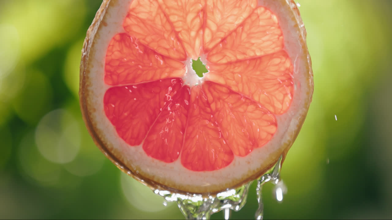 Water Flowing Down Fresh Grapefruit Slice in Slow Motion with Backlit Bright Background