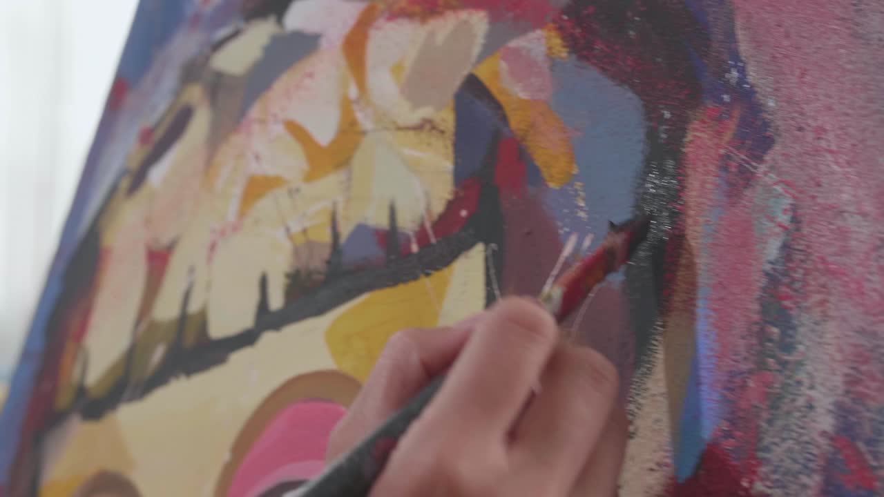 Close-up de uma mão segurando um pincel com cores misturadas e pintando o rosto de uma menina na tela