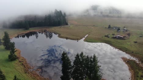 aerial flight by drone over a lake and foggy landscape showing the reflection of clouds