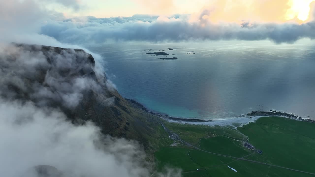 Aerial view of Utakleiv beach in Lofoten under soft midnight sun, calm ocean, clouds, and fog wrapping mountain