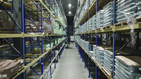 Aerial-Drone-Flight-Down-Warehouse-Aisle-with-Pallet-Racks-and-Forklift-Retrieving-Boxed-Pallet