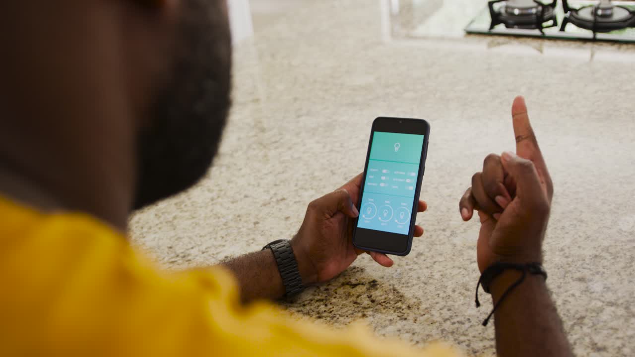 African American man seeing teal app, tapping and adjusting dials, gesturing at kitchen counter