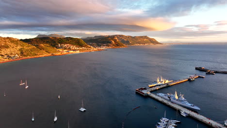 Aerial-cinematic-drone-sunrise-Simon's-Town-naval-boat-marina-fishing-small-quite-city-Cape-Town-South-Africa-early-sunlight-clouds-Table-Mountain-Fish-Hook-Muizenberg-over-bay-backward-movement