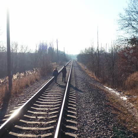 backside view of two boys walking on a rail. children are going along the railroad in a sunny winter day. danger concept.