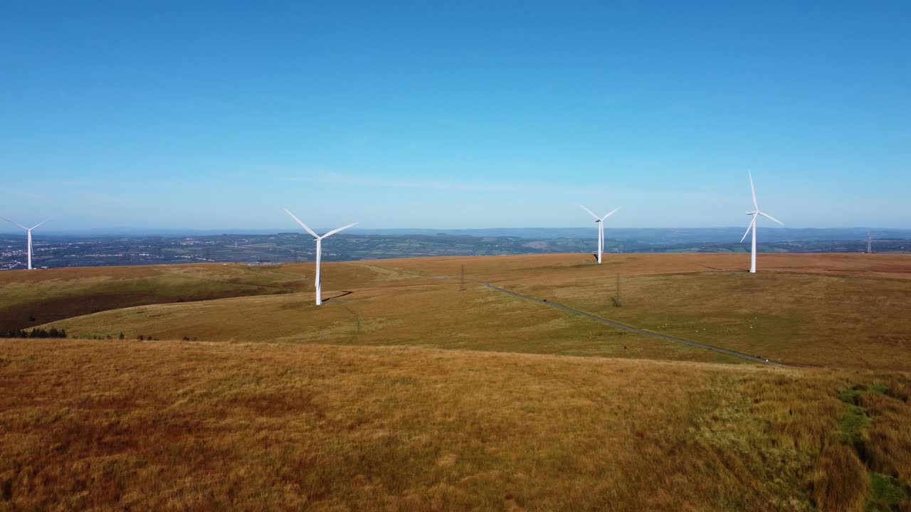 Retreating Drone Aerial Shot of Wind Turbine Farm with Road and Blue Sky Background and Small Pine Tree Forest 4K