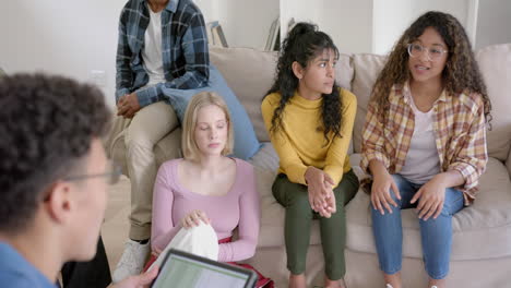 Thoughtful-diverse-group-of-teenage-friends-using-tablet-and-talking-at-home,-slow-motion