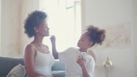 cute girl doing make-up on her mother sitting on couch at home