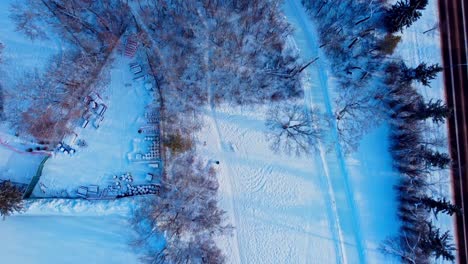 Sobrevuelo-Aéreo-De-Invierno-Reflexión-De-La-Puesta-Del-Sol-Árboles-De-Sombra-Parque-Cubierto-De-Nieve-Almacenamiento-De-Suministros-Área-Cercada-Junto-A-La-Pista-De-Patinaje-Helada-Vacía-Conectada-A-La-Pista-De-Hielo-Artificial-Más-Grande-De-Canadá-En-Edm-Victoria-Park1-6