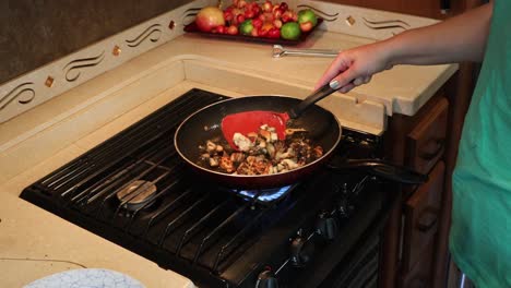 mujer salteando champiñones maitake en una sartén en una pequeña cocina casera