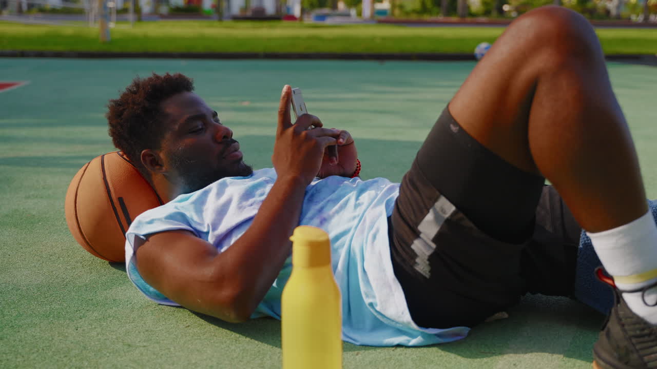 hombre relajándose en la cancha de baloncesto con el teléfono