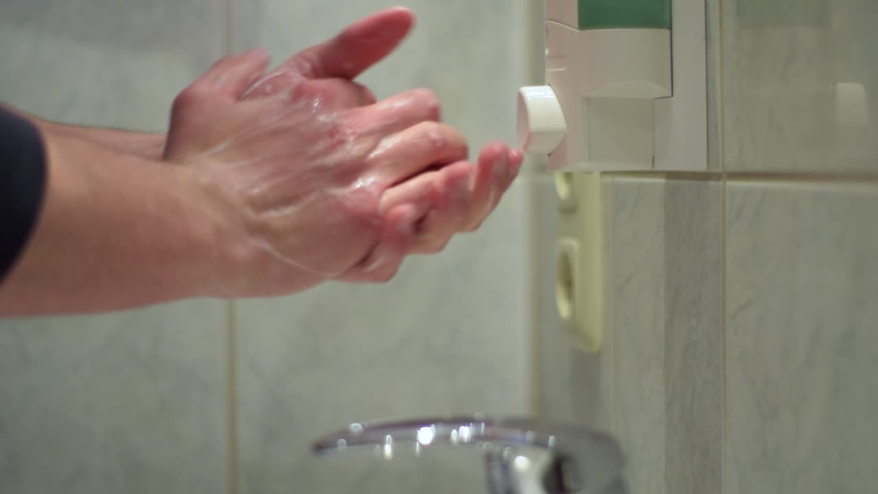 Male hands getting dose of liquid soap out of a dispenser and rubbing it between the hands. Close up.