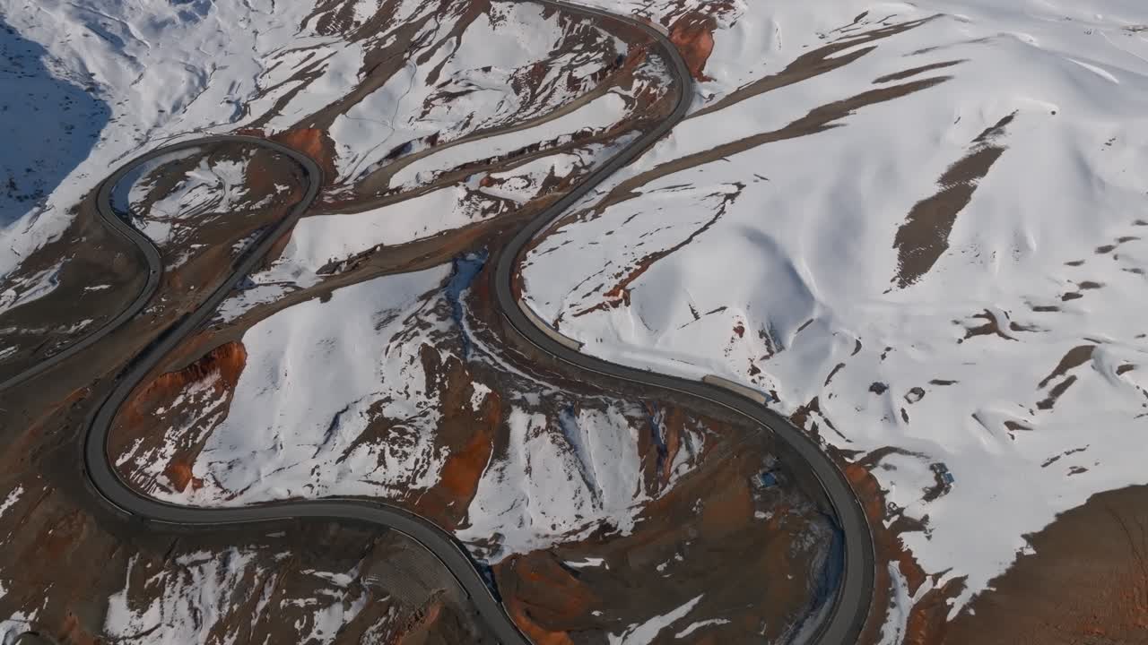 Drone footage of a serpentine mountain highway with sharp hairpin turns across snowy slopes at Chyyyrchyk Pass, Kyrgyzstan, scenic winter travel landscape