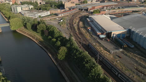 Toma-Aérea-De-Drones-De-La-Casa-Del-Río-Y-El-Museo-Nacional-Del-Ferrocarril-Con-El-Tren-Que-Pasa-Por-La-Estación-De-Tren-De-York-En-La-Soleada-Tarde-De-La-Puesta-De-Sol-Con-árboles-Y-Puente-Peatonal-North-Yorkshire-Reino-Unido