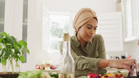 video of happy biracial woman in hijab using smartphone in kitchen