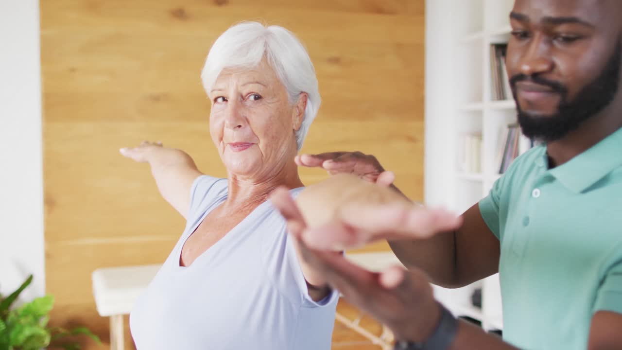 행복한 아프리카계 미국인 남성 물리치료사가 백인 고령 여성과 함께 운동하는 비디오