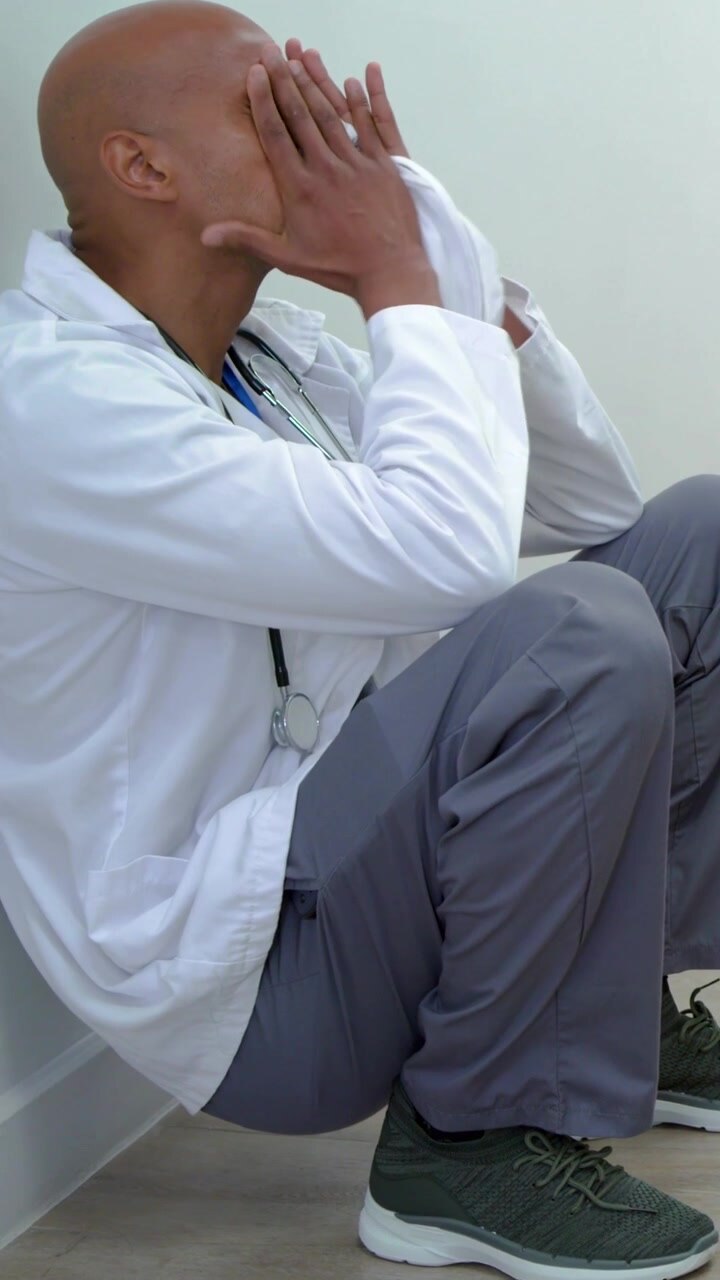Vertical video: Walking scrub team going to X-RAY, white-coated doctor sitting pressing cap tired