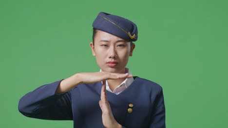 close up of asian woman air hostess looking at camera and showing time out hands gesture while standing in the green screen background studio