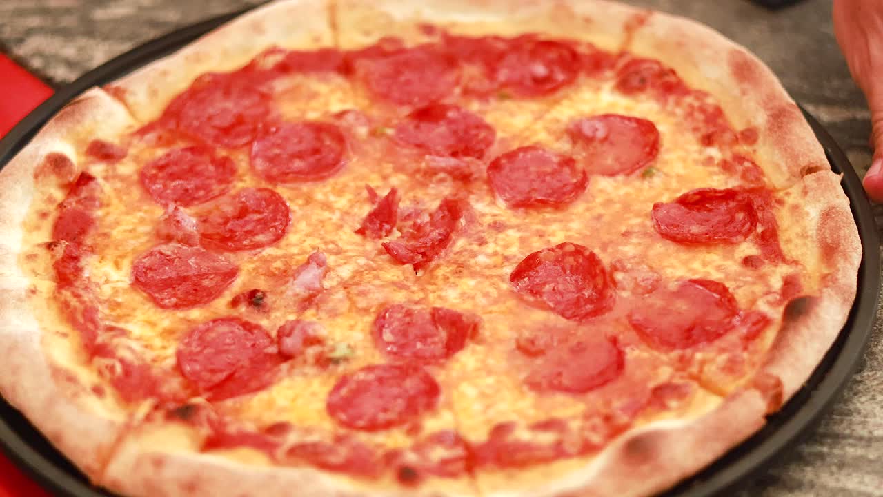 Hands slicing freshly baked pepperoni pizza on table