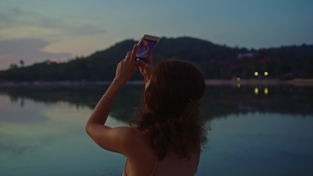 Donna che fotografa il tramonto sul lago
