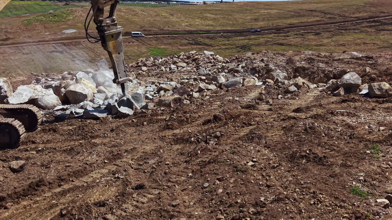 Un operaio edile utilizza macchinari pesanti per frantumare rocce in un cantiere in una zona rurale durante le ore diurne