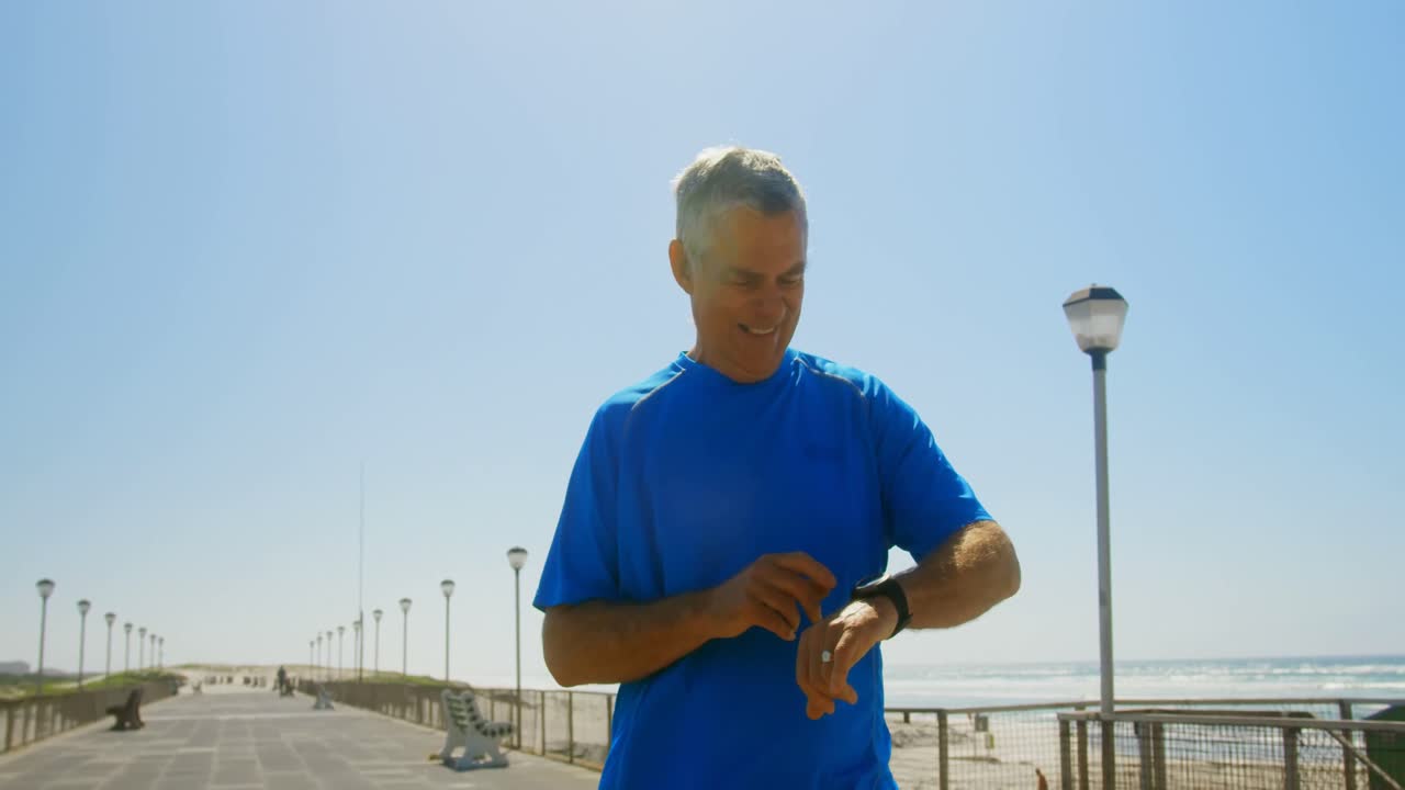 Front view of active senior Caucasian man using smartwatch on a promenade at beach 4k